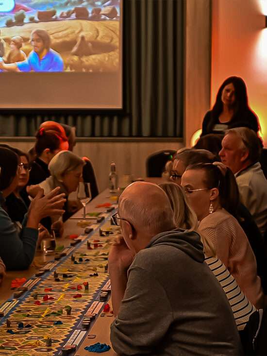 Gäste beim Brettspieleabend im Hotel Huntepadd an langen Tischen mit Spielfiguren und Karten.