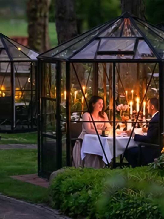 Paar bei einem romantischen Candlelight-Dinner in einem beleuchteten Glashäuschen im Grünen